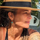 woman with tattoos and hat wearing a golden tassel earring with turquoise stone