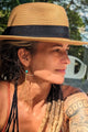 woman with tattoos and hat wearing a golden tassel earring with turquoise stone