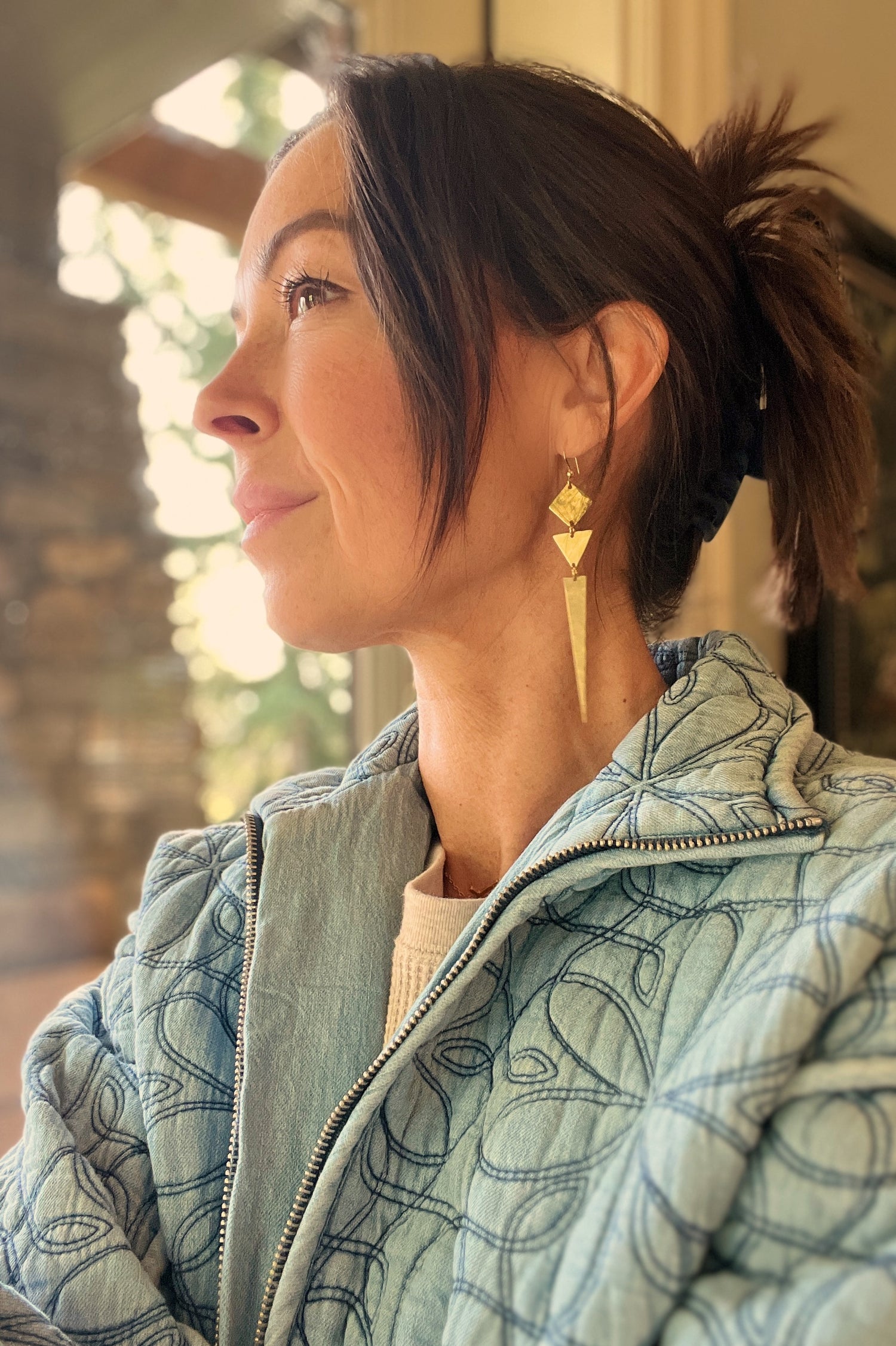 woman wearing golden Geometric dangle earrings and blue quilted jacket