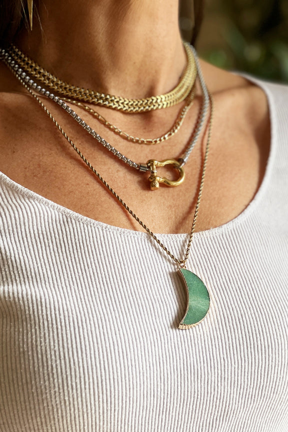 Woman wearing layered gold and silver chunky necklaces with green moon and carabiner 